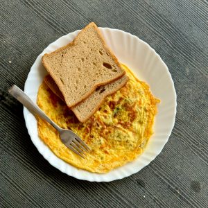 Top view of a toasted bread slice over an omelette on a white plate with a fork.