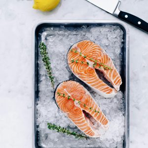 Two fresh salmon steaks seasoned with thyme on ice, accompanied by lemon and knife. Ideal for gourmet recipes.