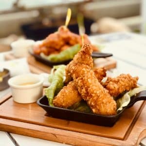 Delicious crispy chicken strips served with a side of sauce on a wooden board.